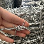 Рука демонстрирует размер и остроту четырехшипового шипа оцинкованной колючей проволоки