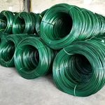Заводской цех, заполненный крупными катушками темно-зеленой стальной проволоки с ПВХ покрытием